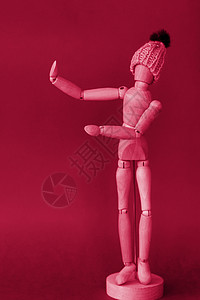 一个戴着针织黄色帽子的男人的木制人体模型指向他旁边的一个地方 红色背景上用木头做的男人的模特娃娃艺术工作成人销售量思考思维颜色生背景图片