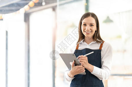 笑容灿烂的女人肖像准备开店迎客咖啡店的老板正在等待开店 心甘情愿地等待为客户服务店铺企业家围裙职业本生意商业人士招牌成人餐厅背景图片