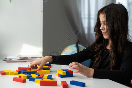 一个小女孩在桌边玩棋盘游戏 用木制立方块建造一座塔高清图片