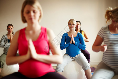 一群孕妇幸福的母性 一群多民族的孕妇在瑜伽课上用健身球进行冥想背景