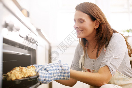 一个成熟的女人从烤箱里拿了熏肉出来 感觉很爽吧?高清图片