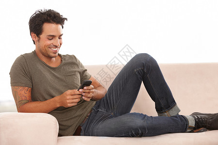 有些消息只会让你微笑 一个英俊的年轻人在沙发上放松 用他的 mp3 播放器听音乐背景图片