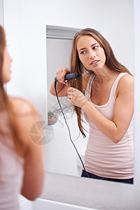 有个女人在头发上用平板铁烫着她的头发皮肤裁剪黑发房子微笑女性浴室成人背景图片