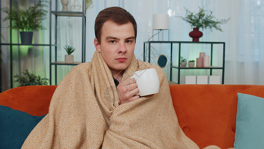 冷的发抖生病的少年男子戴着格子花呢帽子 独自坐在沙发上喝着热茶 冷得瑟瑟发抖背景