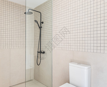 带白色马桶盖的小浴室和带透明玻璃墙的封闭式淋浴区 由不同形状的米色瓷砖制成的墙壁相互和谐地组合在一起图片