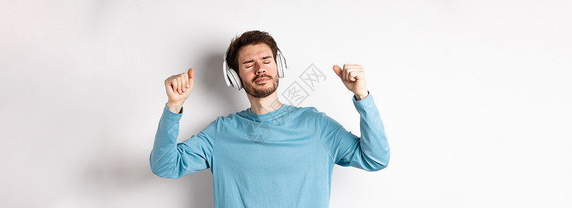 快乐的英俊男子跳舞 用耳机音乐 听歌和微笑 站在白色背景上胡子广告商业成人工作室胡须生活办公室促销发型背景图片