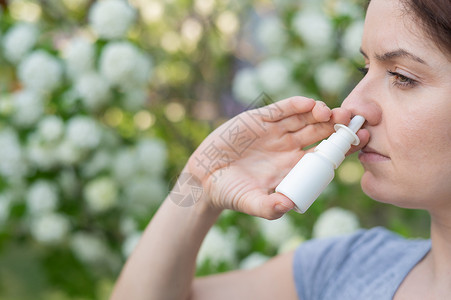 吹尘器白种女人在公园散步时用鼻涕喷雾瓶子鼻孔花粉液体药物治疗疾病鼻子呼吸喷嚏背景