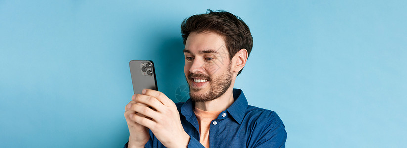 魅蓝手机素材观看移动屏幕和微笑 站在蓝背景上 校对商业男人电话技术情绪手机胡须发型成功胡子背景