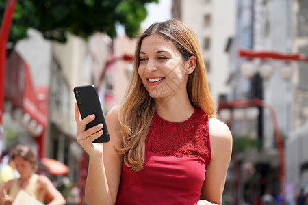 在圣保罗市行走的有吸引力 微笑着笑容的妇女肖像 在背景模糊的移动电话上发短信技术邻里女士晴天美女城市生活方式喜悦休闲幸福背景