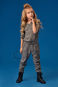 穿着时装长卷发的小女孩 穿着时尚服装童年忧郁乐趣消费者衣服套装顾客蓝色金发女郎靴子背景图片