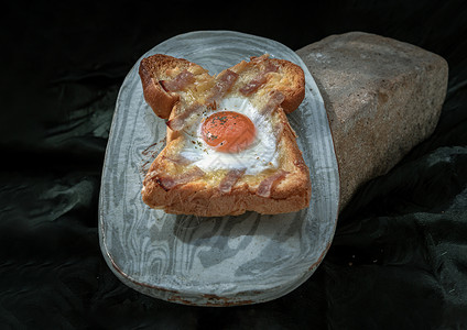 培根蛋面黑底陶瓷盘上的烤培根和奶酪烤面包里自制的炸鸡蛋背景美食奶油甜点食物深色蛋黄岩石糕点石头背景