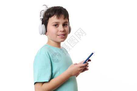 梦回少年文字手持手机 可爱地笑着对着摄影机微笑的画面; 在智能少年男孩戴耳机的白色背景上的孤立肖像背景