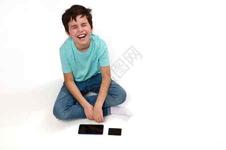 一位不满的高加索男孩最乐观的景象 带着智能手机和信用卡坐在白色背景的白种背景上表示悲伤背景图片