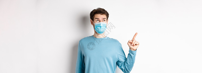 Corona病毒 健康和检疫概念 戴医疗面具的好奇者 用左上角的横幅指向和看着左上角 站在白色工作室背景上成人快乐促销胡须口罩男背景图片