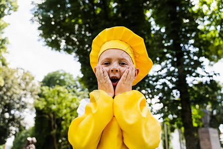 穿着黄色厨师帽子和围裙穿黄色制服的厨艺儿童被吓得脸颊惊呆 在户外出人意料童年活动公园面包师乐趣食物男生厨房孩子们面包背景图片