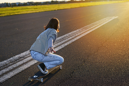 骑乐无穷美丽的亚洲女孩在滑板上的侧视图 在空旷的道路上骑着她的巡洋舰向着太阳 快乐的年轻溜冰者在她的溜冰鞋上享受阳光明媚的一天长板女性乐背景
