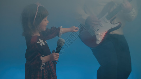穿旧礼服的小女孩在舞台上唱歌 她父亲弹电吉他电吉他彩色复古才俊戏服蕾丝金属裙子衣服背景背景图片