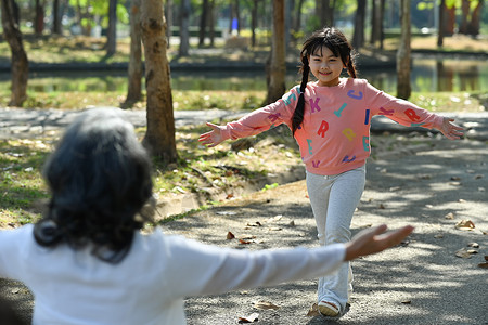 万国来朝爱祖母伸出双臂在公园里向她跑去 同时微笑着孙女朝她跑来 家庭与爱情概念背景
