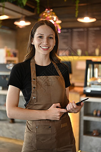 在现代咖啡馆的柜台前微笑着笑着向摄影机微笑的年轻女酒吧女记者肖像背景