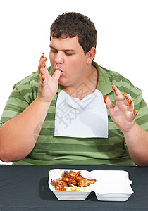 手指全是肥肉 一个肥胖的年轻人戴着围嘴 坐在一张桌子旁 桌子上放着一盒鸡翅 舔着沾满酱汁的手指背景图片