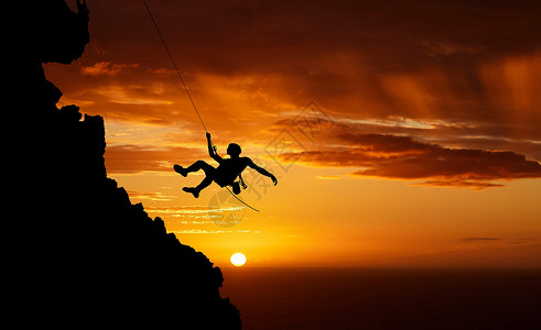 悬崖人日落天空绳降 山的轮廓和徒步旅行的人挂在影子绳上 健身风险 冒险自由挑战和强烈 超现实的自然肾上腺素和在橙色景观上攀登悬崖背景