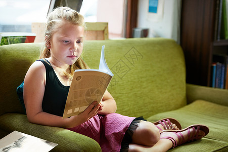 有个可爱的金发女孩在沙发上放轻松 写着一本好书背景图片