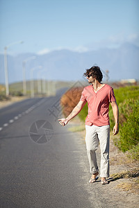 一个年轻人在一条废弃的路上走着搭便车 想搭个顺风车呢 笑声男性假期天空冒险闲暇远足货车旅行游客吉普车背景