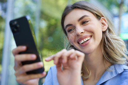 坐在街上户外的美丽的年轻女士 对智能手机微笑 在网上购买 移动电话订单面试高清图片素材