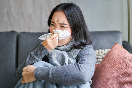 找到家感觉韩国女孩在午睡时打喷嚏 围着围巾坐在家里 感觉不舒服 冬天的概念 取暖费和人的特写房子流感成人疼痛药品互联网沙发毯子温度症状背景
