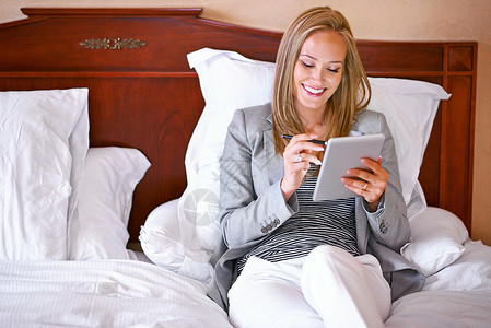 一名年轻女商务人士在卧室里用数码平板电脑做客 现在她已经进入她的套房进行在线检查背景图片