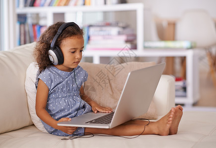 她已经是个小天才了 一个小女孩坐在家里时 使用耳机和笔记本电脑背景图片