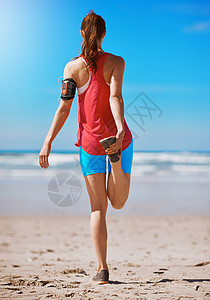 只跑一次伸展是每一次锻炼的重要部分 一个年轻女人在跑到海滩之前被重新瞄准的镜头拍下来了背景