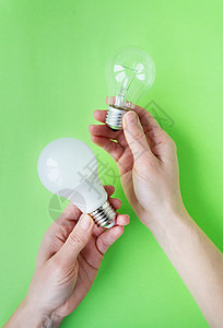 LED和白月灯是两类灯具 放在一个女孩的手中 她被隔离在绿色背景上 节能灯背景图片