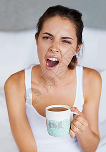 打个哈欠一名年轻女子在床上坐在一杯咖啡里打大哈欠时 用咖啡洗了睡梦中的一些咖啡背景