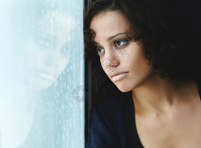 忧郁的阴暗面 一个悲伤的年轻女人坐在窗边 外面下着雨背景