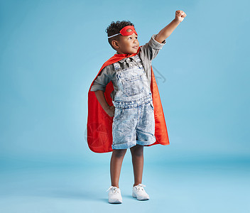 穿着超级英雄斗篷的勇敢快乐男孩 并用面具遮住他假扮蓝背景飞行的拳头 强壮的孩子准备用超能力拯救世界背景图片