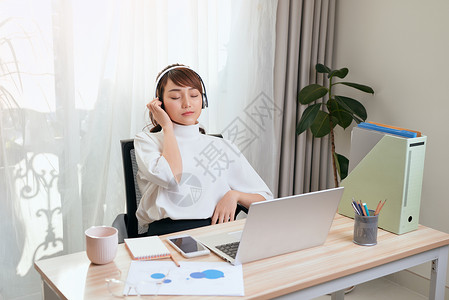 放松的亚洲年轻女性在工作时 在桌边听音乐快乐技术电脑耳机媒体演讲女士专业自由职业者见面会背景图片