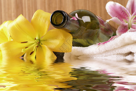 瓶子里的百合温泉水背景的瓶装按摩油芳香香气花瓣疗法竹子治疗白色毛巾反射黄色背景