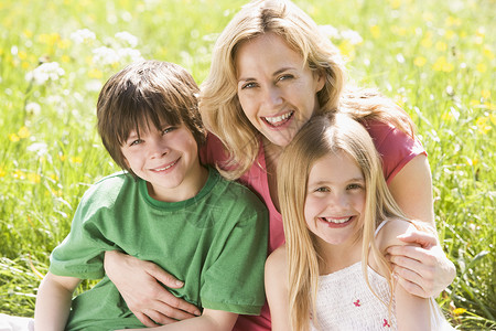 年幼的女孩母亲和两个年幼的孩子坐在户外微笑背景