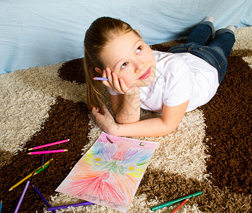女孩躺在地毯上 深思熟虑地画出彩笔和照片背景图片