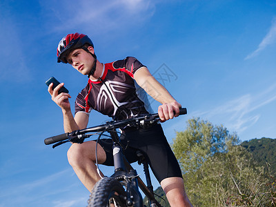 拥有电话骑山上自行车的青年男子骑术技术阅读男人低角度短信运动互联网成人消息背景图片
