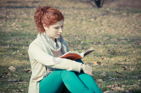 公园里的红长头发女孩在看书红色头发复古裤子季节读书绿色背景图片