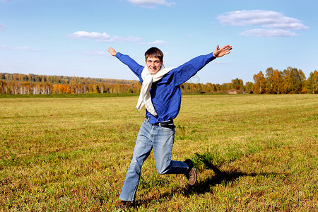快乐的少年跑草地衬衫深色青少年天际牛仔裤地平线树木蓝色阳光背景图片
