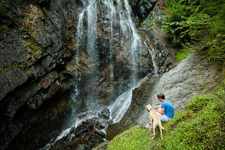 在瀑布附近带狗的年轻人高清图片