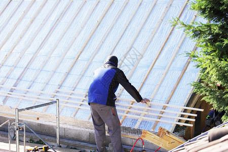 盖屋顶人屋顶在木柴新屋顶上工作瓦工男性工匠房子天空工具锤子劳动者工艺住房背景