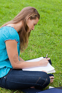 盘腿而坐的学生严肃的年轻女孩在她笔记本上写作时坐着背景