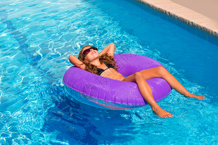 紫色太阳镜女孩在紫充气泳池环上放松紫色戒指太阳微笑假期比基尼享受闲暇眼镜童年背景