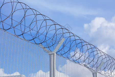 蓝色天空下带刺铁丝网的连链围栏外壳栅栏倒钩防御安全螺旋障碍监狱金属网格背景图片