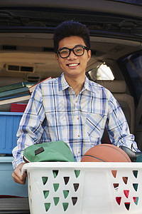 篮球衣号码汽车后面有大学宿舍用品的男孩肖像眼镜面包车校园大学生学习学生头发衣篮后备箱棕色背景