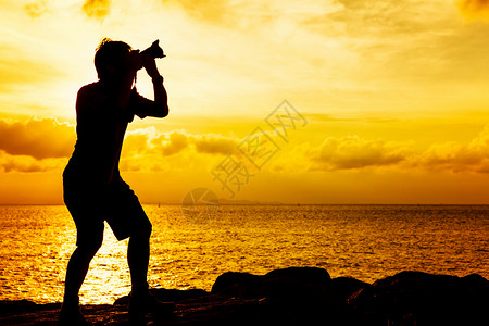 日落时摄影师的轮光岩石男人太阳男性单人照片三脚架海岸相机海洋背景图片